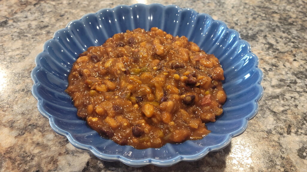 Homemade Southern baked beans with bacon and black beans served in a blue bowl.